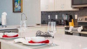 A modern kitchen with white cabinets, a large island with glassware, and a painting on the wall. - Stunning 2Bd Apto Close to Disney Storey Lake 105 3171 (Kissimmee)