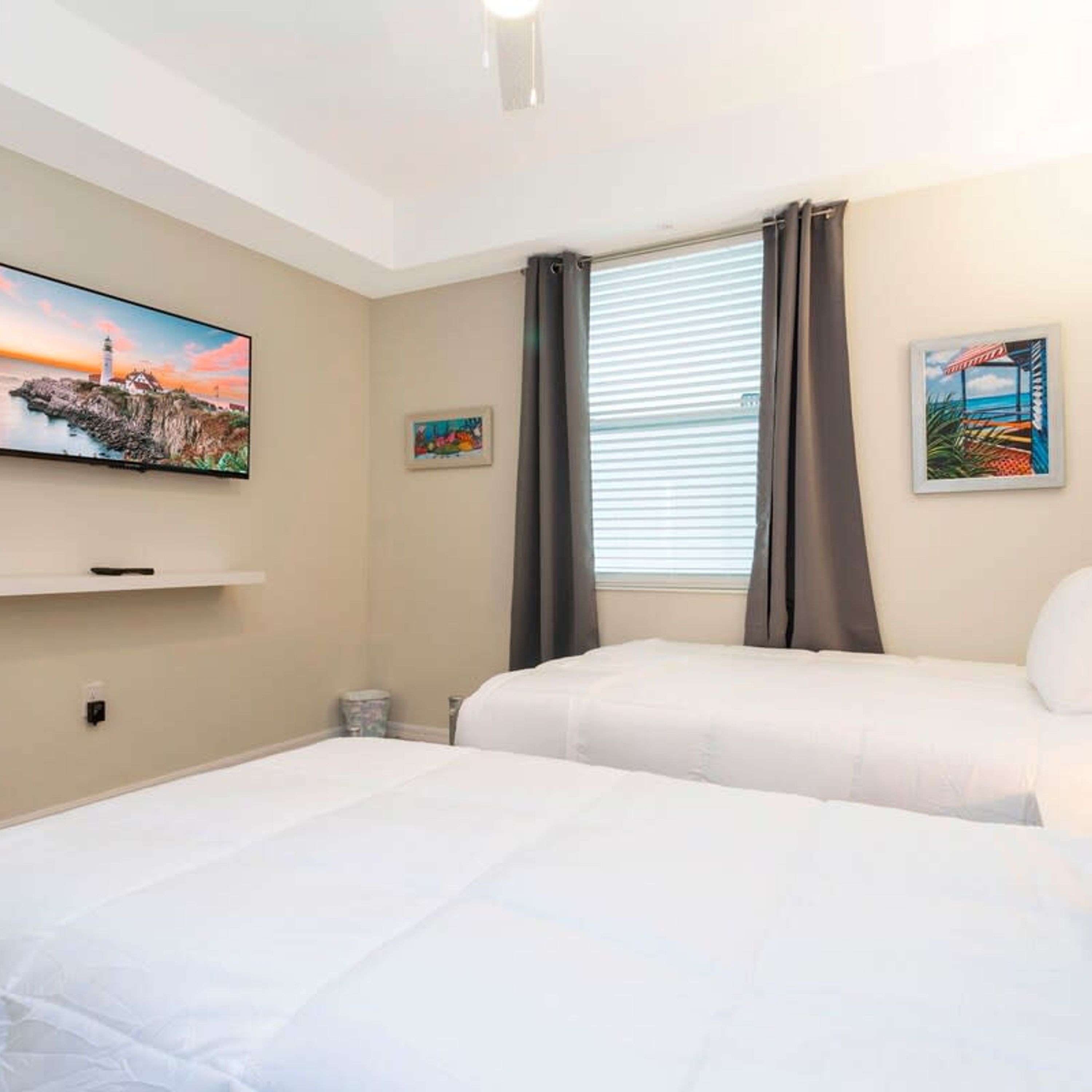 A hotel room with two beds, a TV mounted on the wall, a window with curtains, and artwork on the walls.