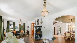 A spacious living room with a fireplace, a dining area, and a kitchen visible through an archway. - The Ella Norah. A Luxury Retreat. Pool and Spa. Steps to Main Street.  (Smithville)