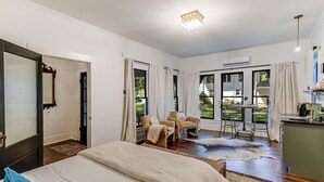 A spacious bedroom with a large bed, a sitting area with chairs, and a view of the outdoors through large windows. - The Ella Norah. A Luxury Retreat. Pool and Spa. Steps to Main Street.  (Smithville)
