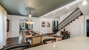 A spacious dining area with a large table and chairs, a chandelier, and a staircase with a black railing. - The Ella Norah. A Luxury Retreat. Pool and Spa. Steps to Main Street.  (Smithville)
