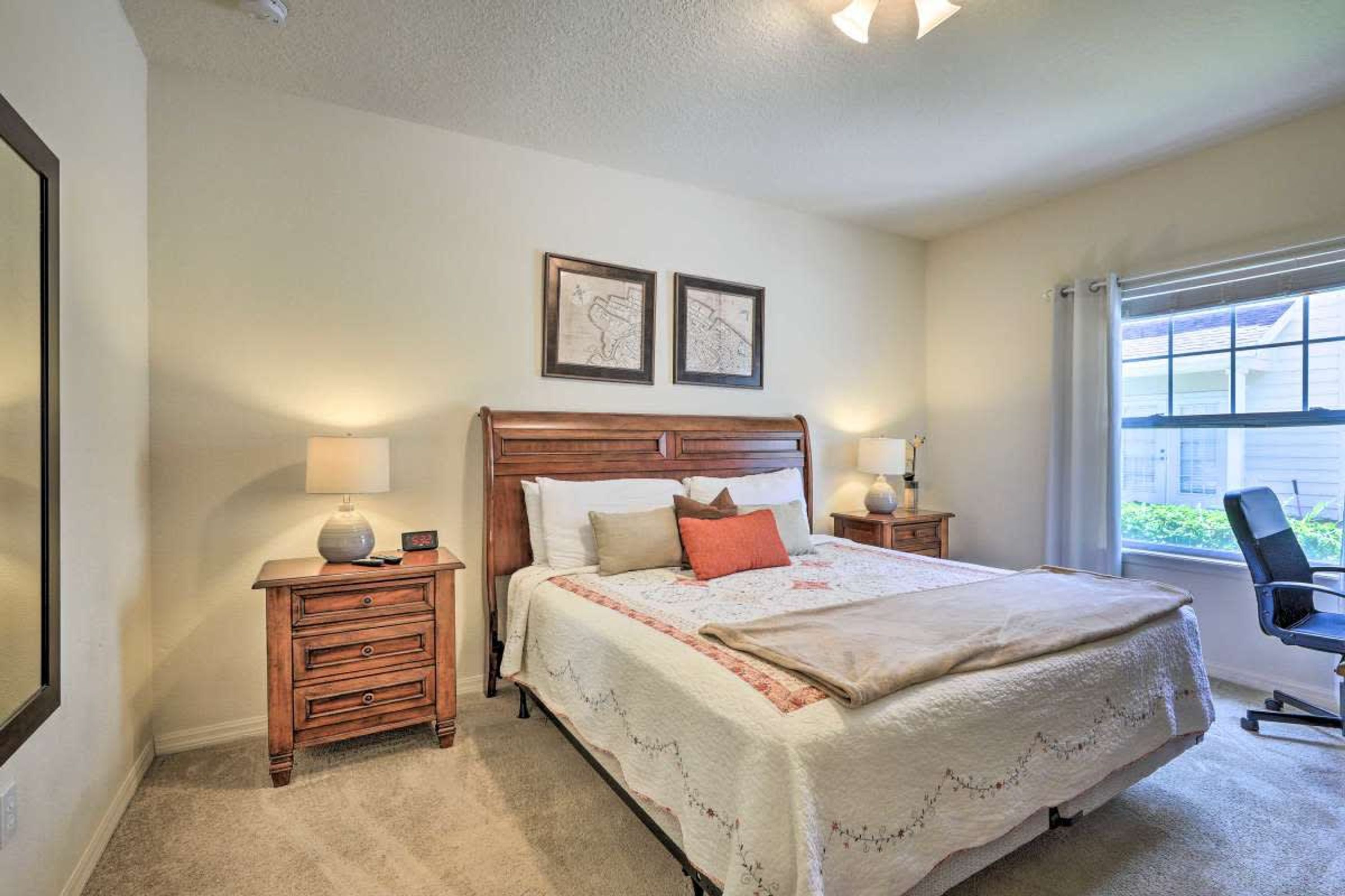 Une chambre à coucher avec un grand lit, deux tables de chevet avec des lampes, une commode en bois et deux tableaux encadrés accrochés au mur.