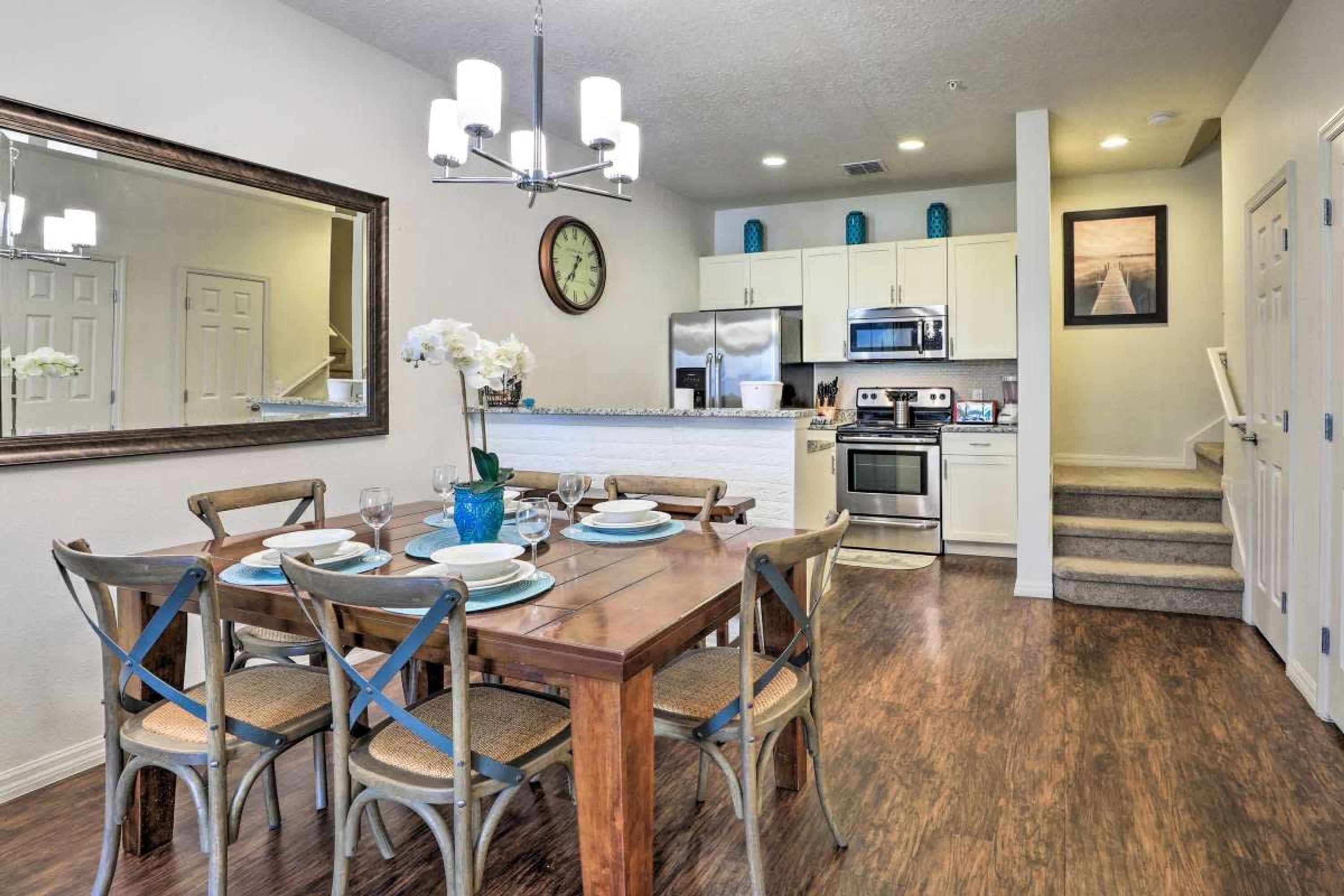 A dining area with a wooden table and chairs, a large mirror, and a clock on the wall.