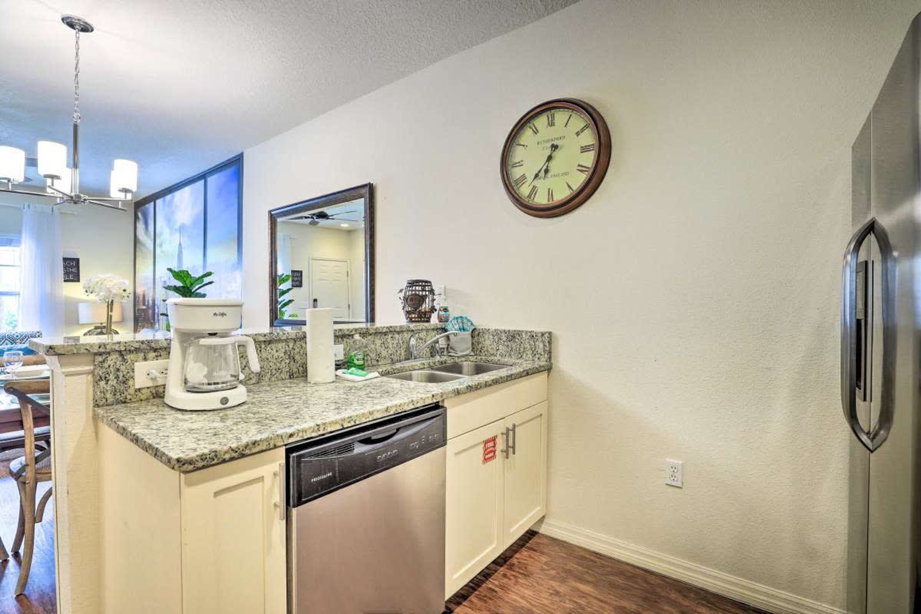 Una cocina con encimera de granito, lavavajillas de acero inoxidable y un reloj en la pared.