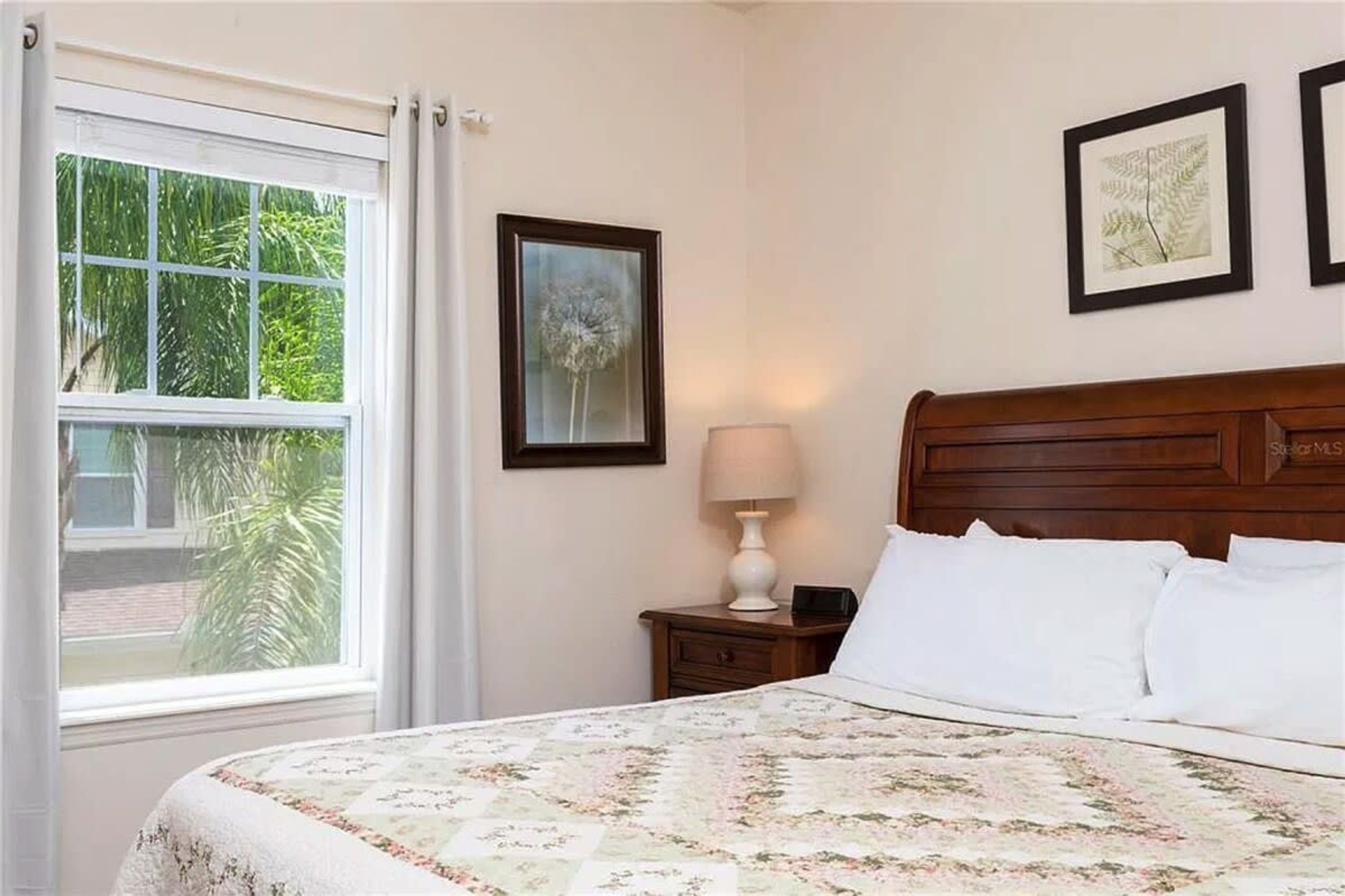 A bedroom with a bed, a nightstand, a lamp, and framed pictures on the wall.