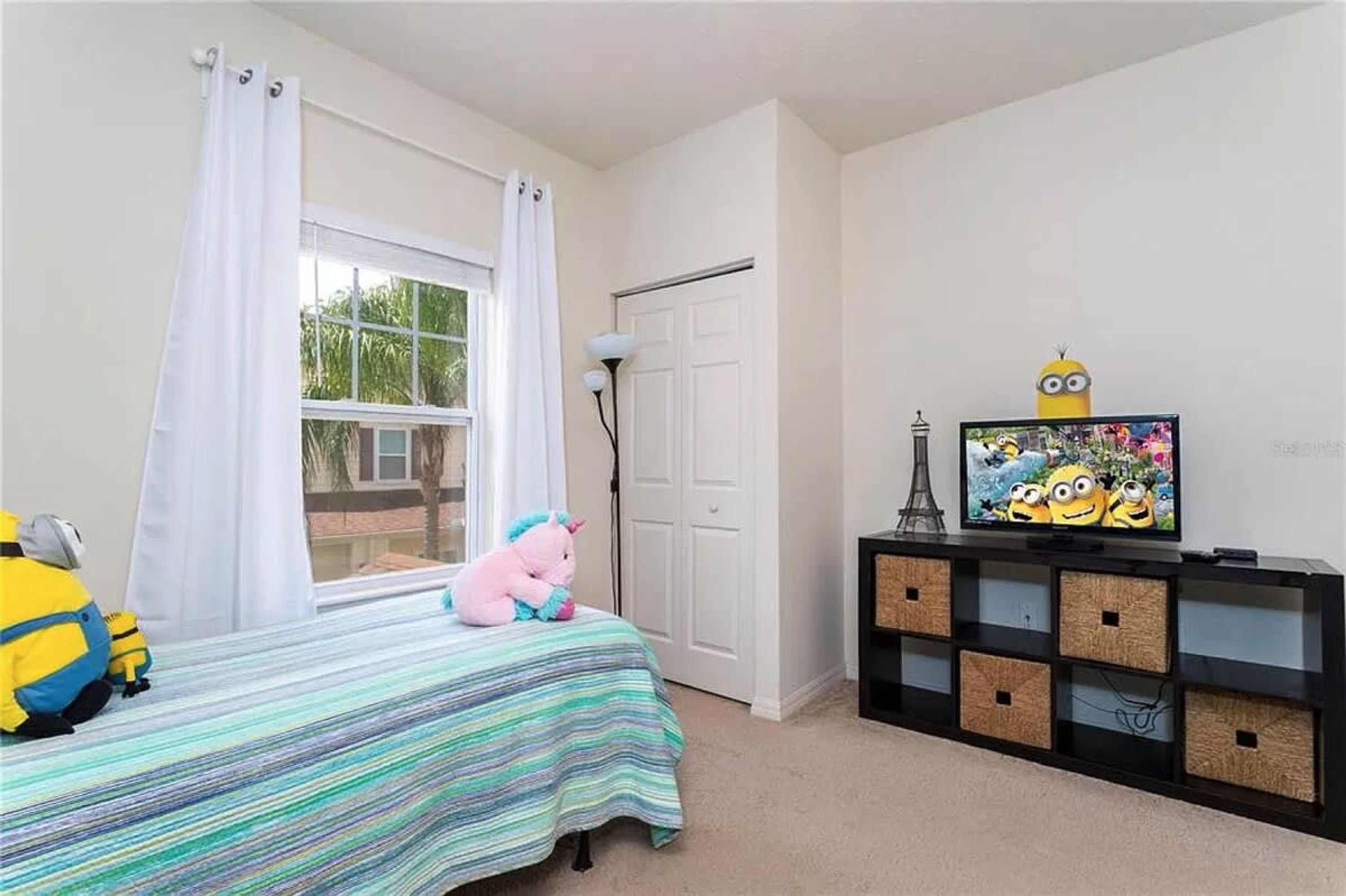 A bedroom with a bed, a window with curtains, a television, and a Minion-themed decoration.