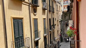Une rue étroite, bordée de bâtiments des deux côtés, avec des balcons ornés de balustrades et de plantes en pot.