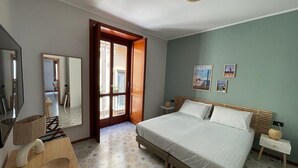 Une chambre à coucher avec un lit, une table de chevet en bois, un miroir, une porte donnant sur une autre pièce et un mur orné de deux tableaux encadrés.