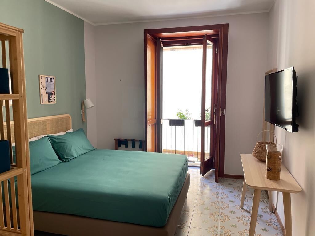 Een slaapkamer met een bed, een televisie, een klein tafeltje en een balkondeur.