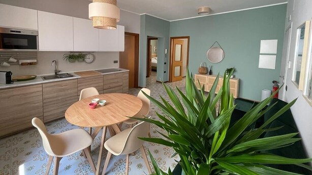 Une cuisine moderne avec une table à manger ronde et des chaises, un luminaire suspendu et une grande plante verte au premier plan.