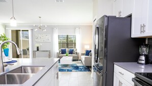 A modern kitchen with a large island, stainless steel appliances, and a dining area with a sofa and coffee table. - Stunning 5 Bd w Pool Close to Disney Champions Gate 1012 (Davenport)