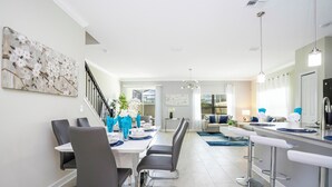 A modern dining area with a long table, bar stools, and a staircase leading to another level. - Stunning 5 Bd w Pool Close to Disney Champions Gate 1012 (Davenport)