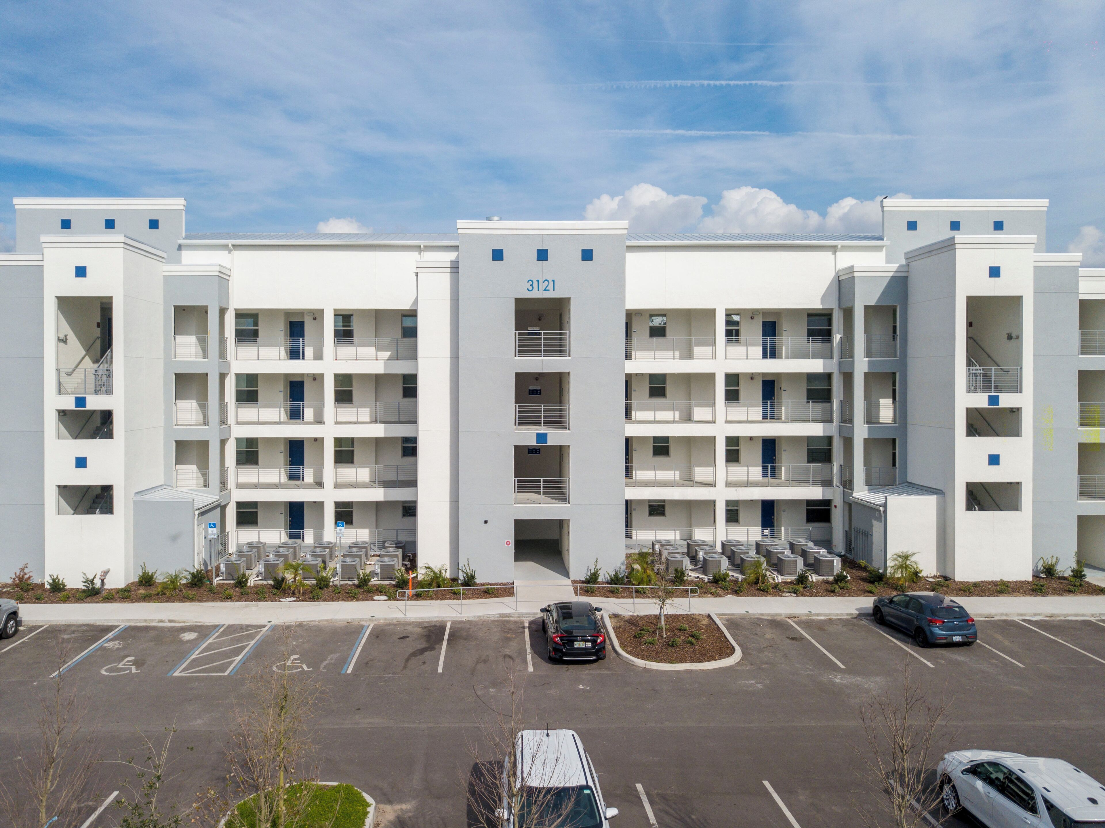 A modern multi-story building with a flat facade, numbered 3121, featuring a central entrance and multiple balconies.