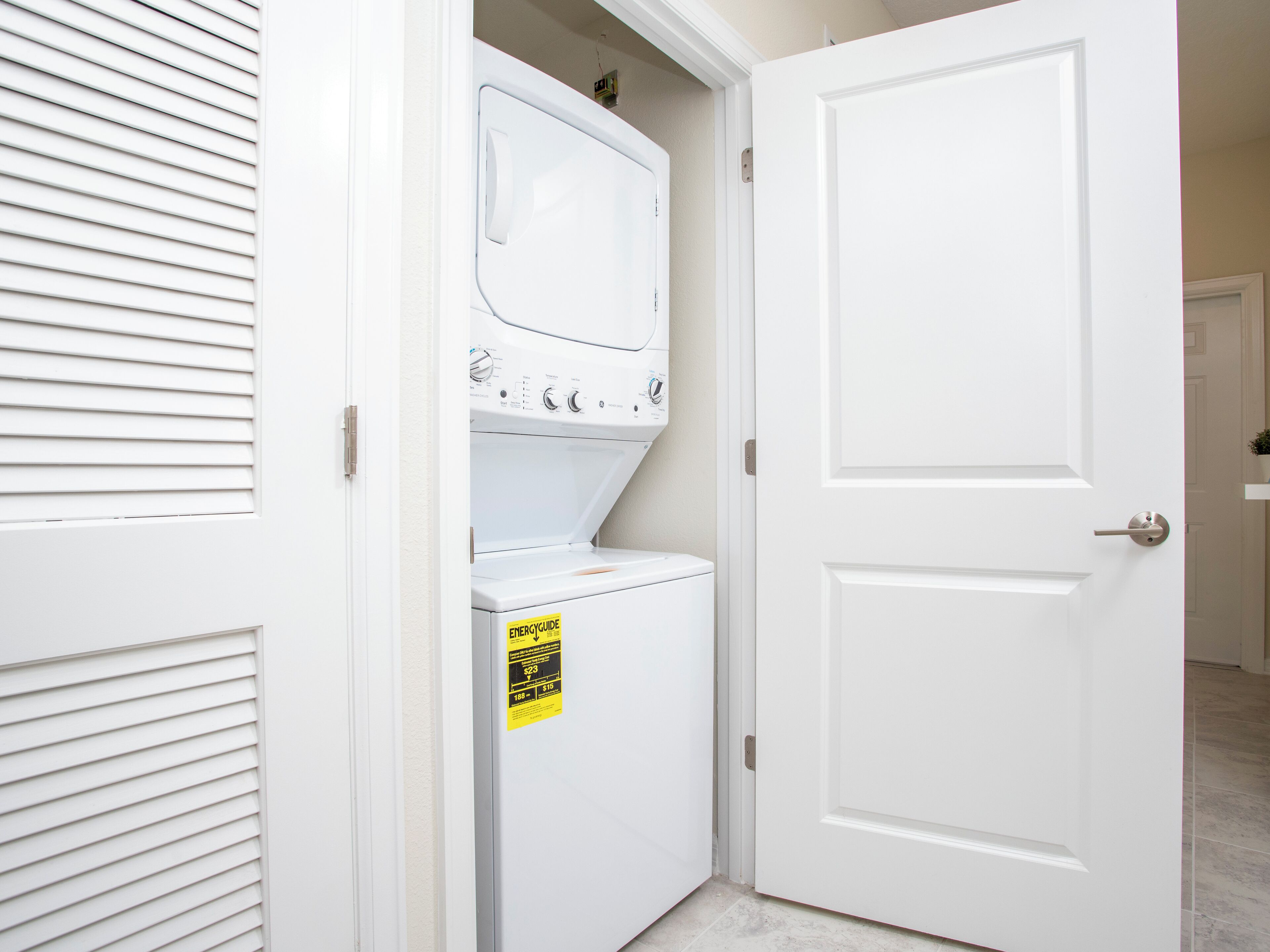A laundry room with a front-loading washer and dryer, a door with a lock, and a small sign on the dryer.