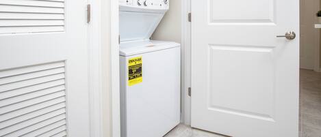 Uma lavanderia com máquina de lavar e secadora frontais, uma porta com fechadura e uma pequena placa na secadora.