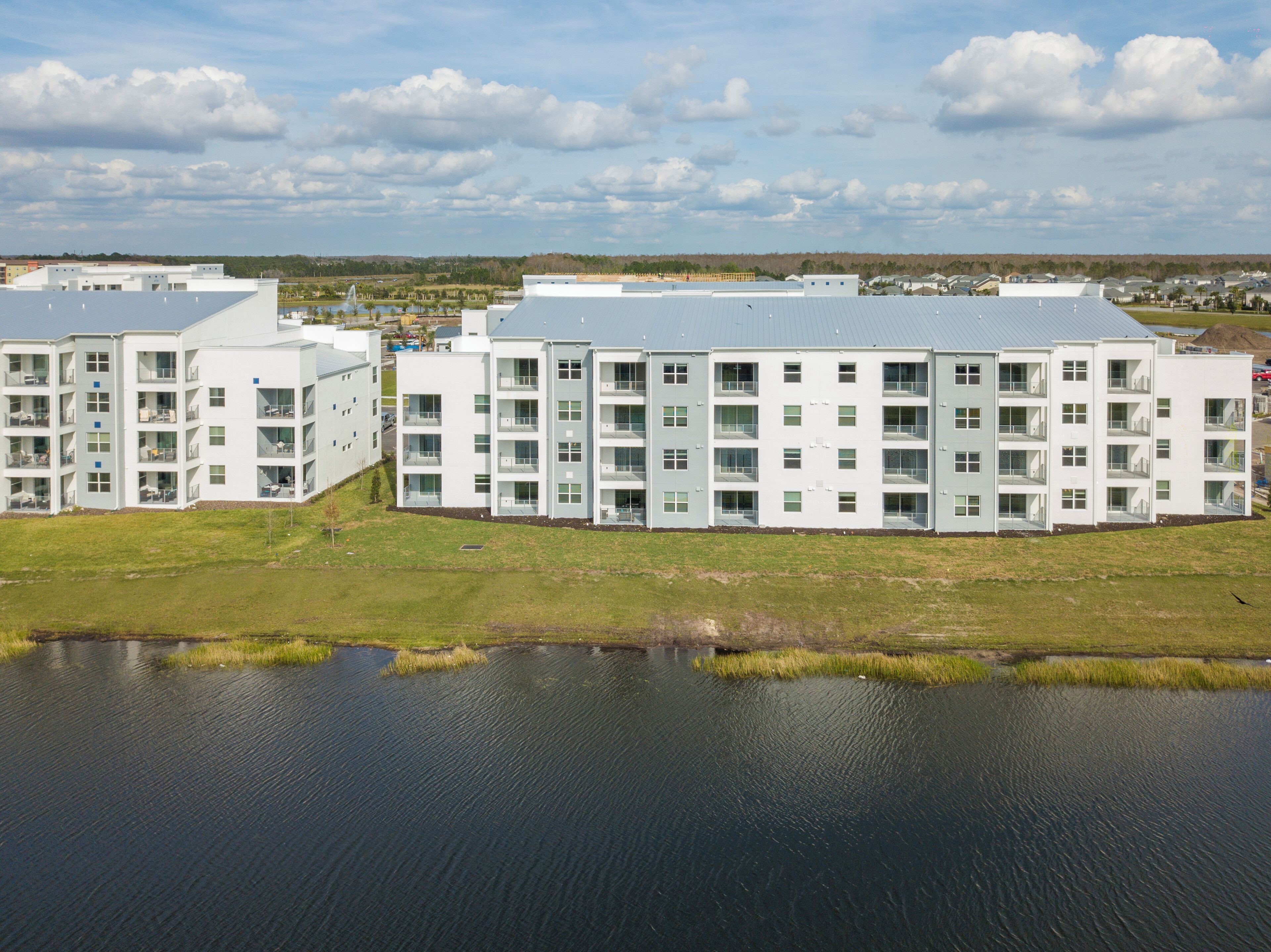 A modern multi-story building with a flat roof, surrounded by a body of water and grassy areas.