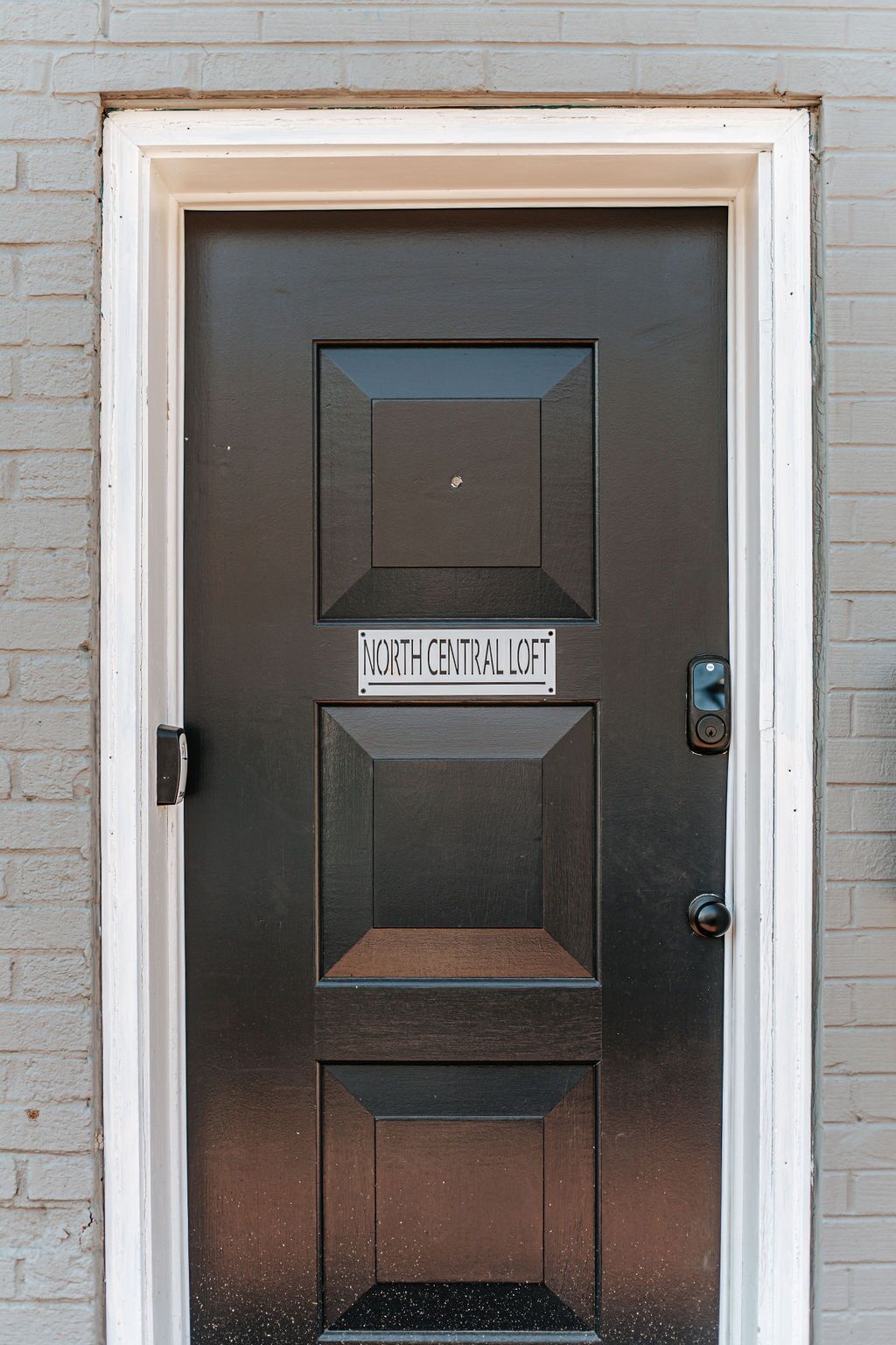Una puerta marrón oscuro con un letrero que dice 'North Central Loft' sobre una entrada hundida.