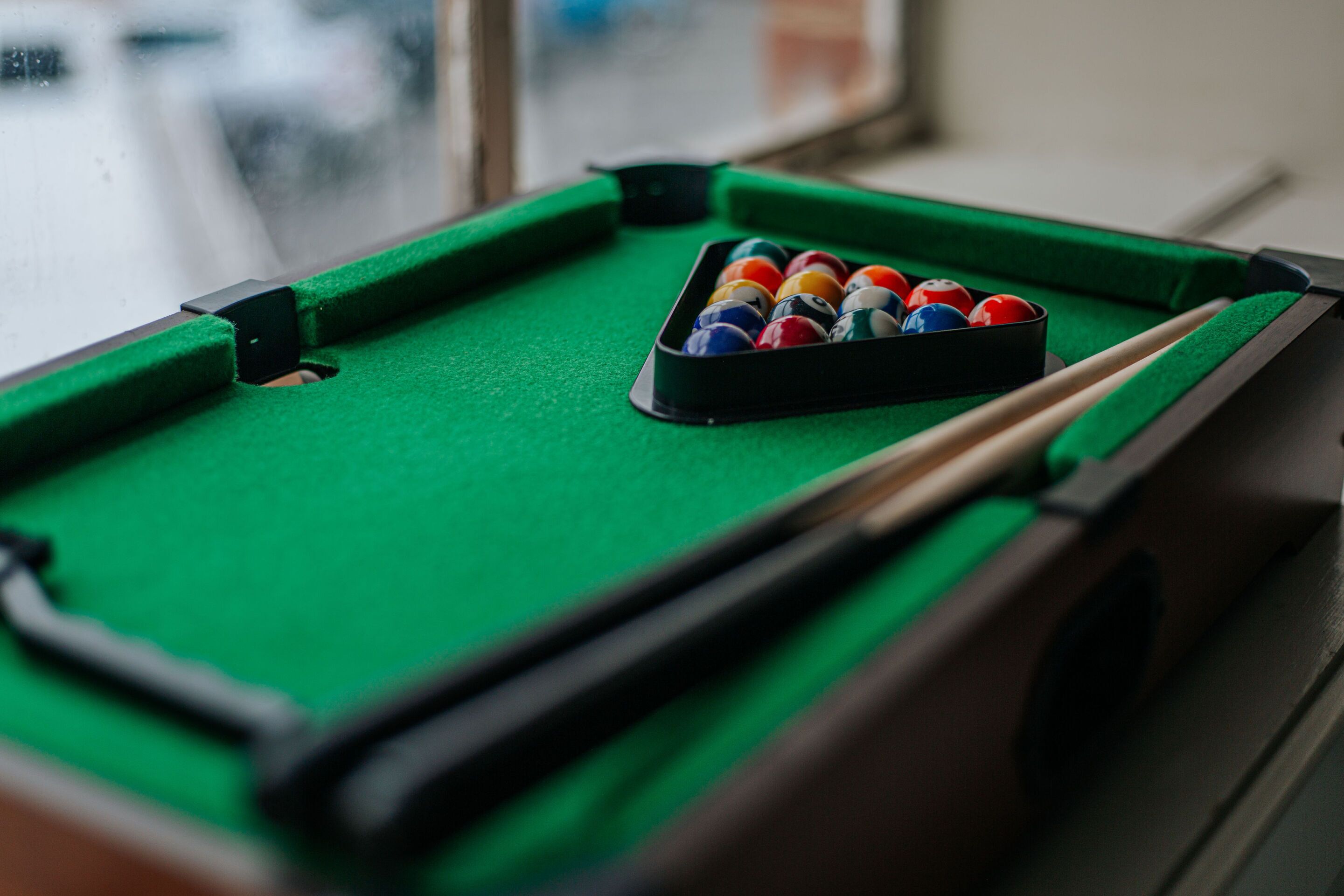 A pool table with a green felt surface and a set of pool balls in a rack.