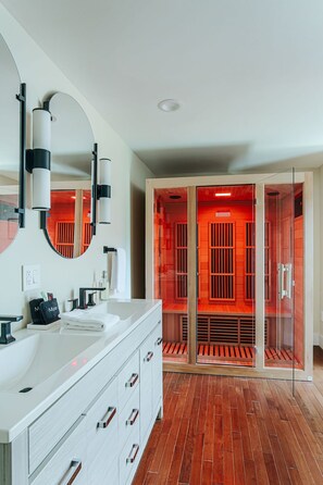 A modern bathroom with a white vanity, a large mirror, and a glass-enclosed walk-in closet with red lighting. - North Central Loft (Staunton)