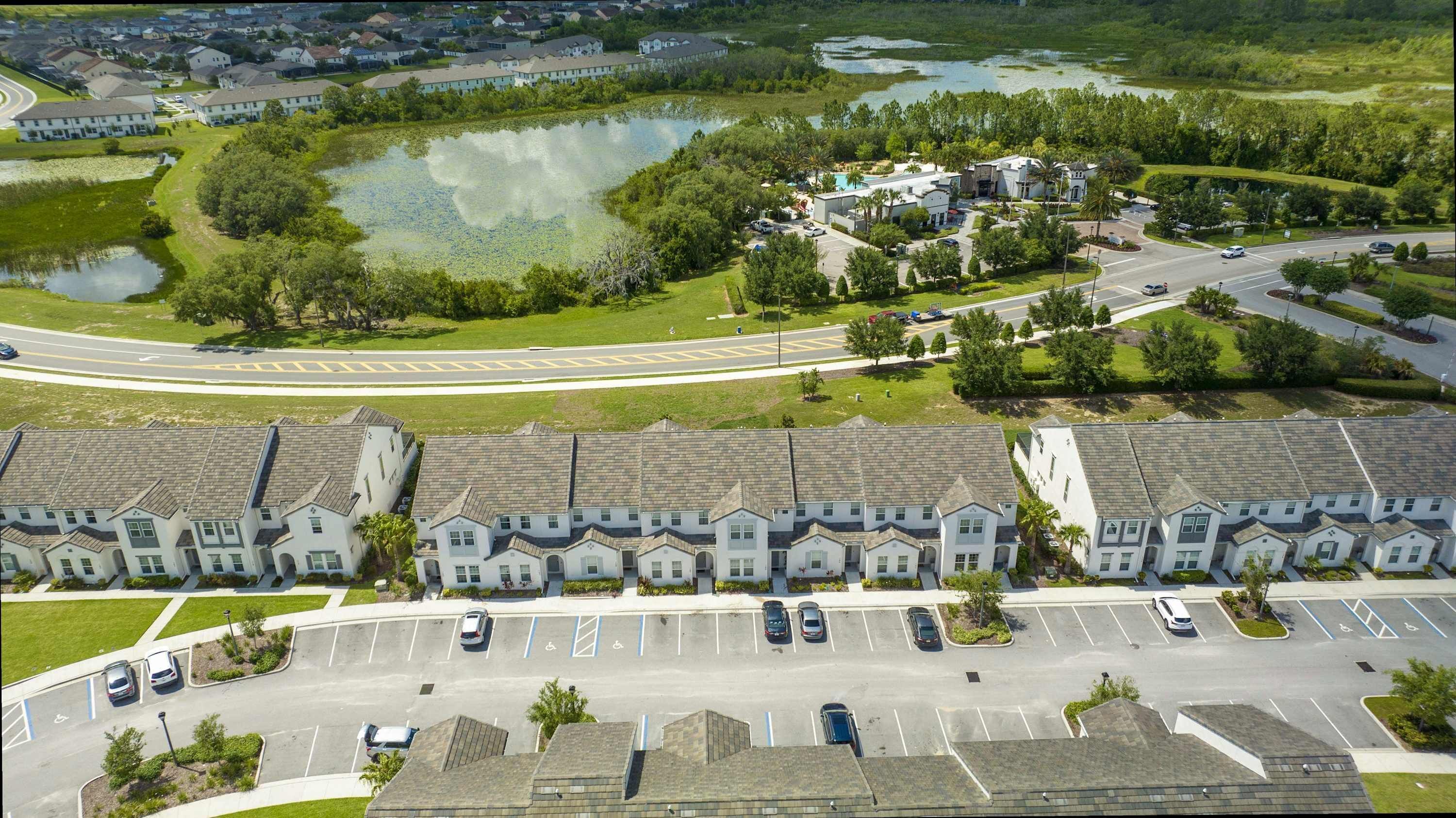 A residential area with a row of townhouses, a parking lot, and a body of water.
