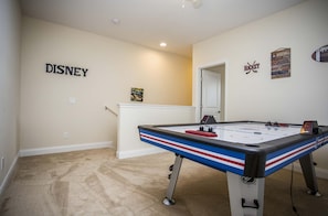 Et værelse med et billardbord, en dør der fører til et andet rum, samt vægdekorationer, herunder skilte med 'DISNEY' og 'Hockey'.