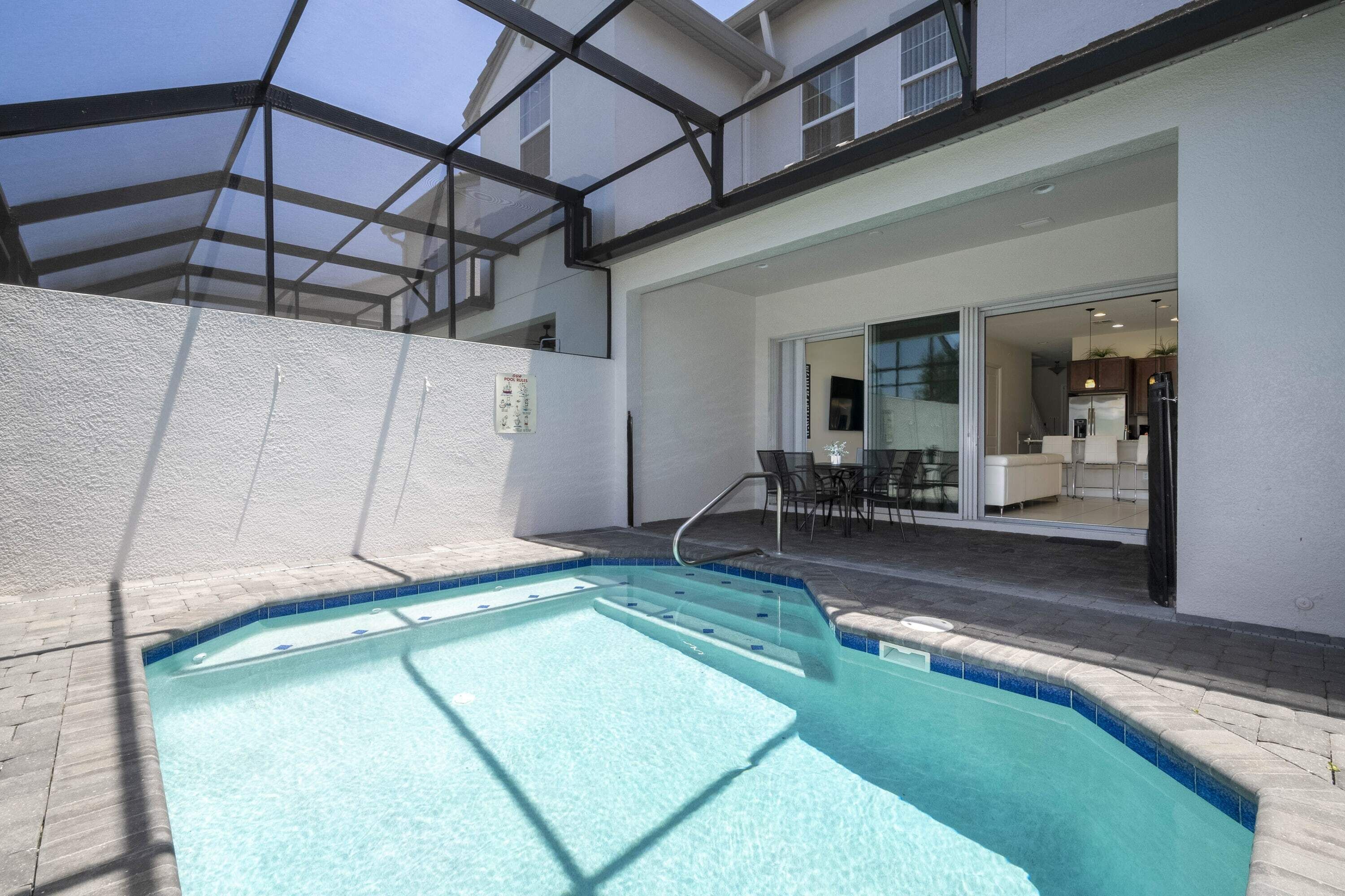 A swimming pool with a glass ceiling, a patio area with outdoor furniture, and a view into a modern interior space.