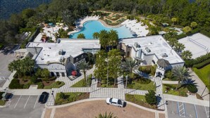 Vue aérienne d’un complexe hôtelier avec une piscine, des palmiers et un parking.