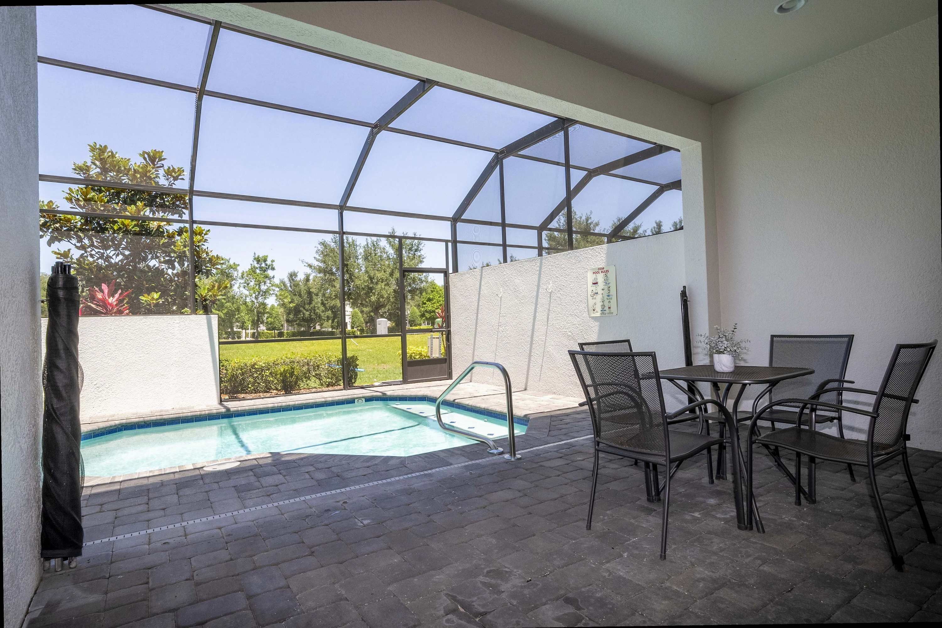 En overdækket terrasse med swimmingpool, udendørs møbler og udsigt til grønne omgivelser.