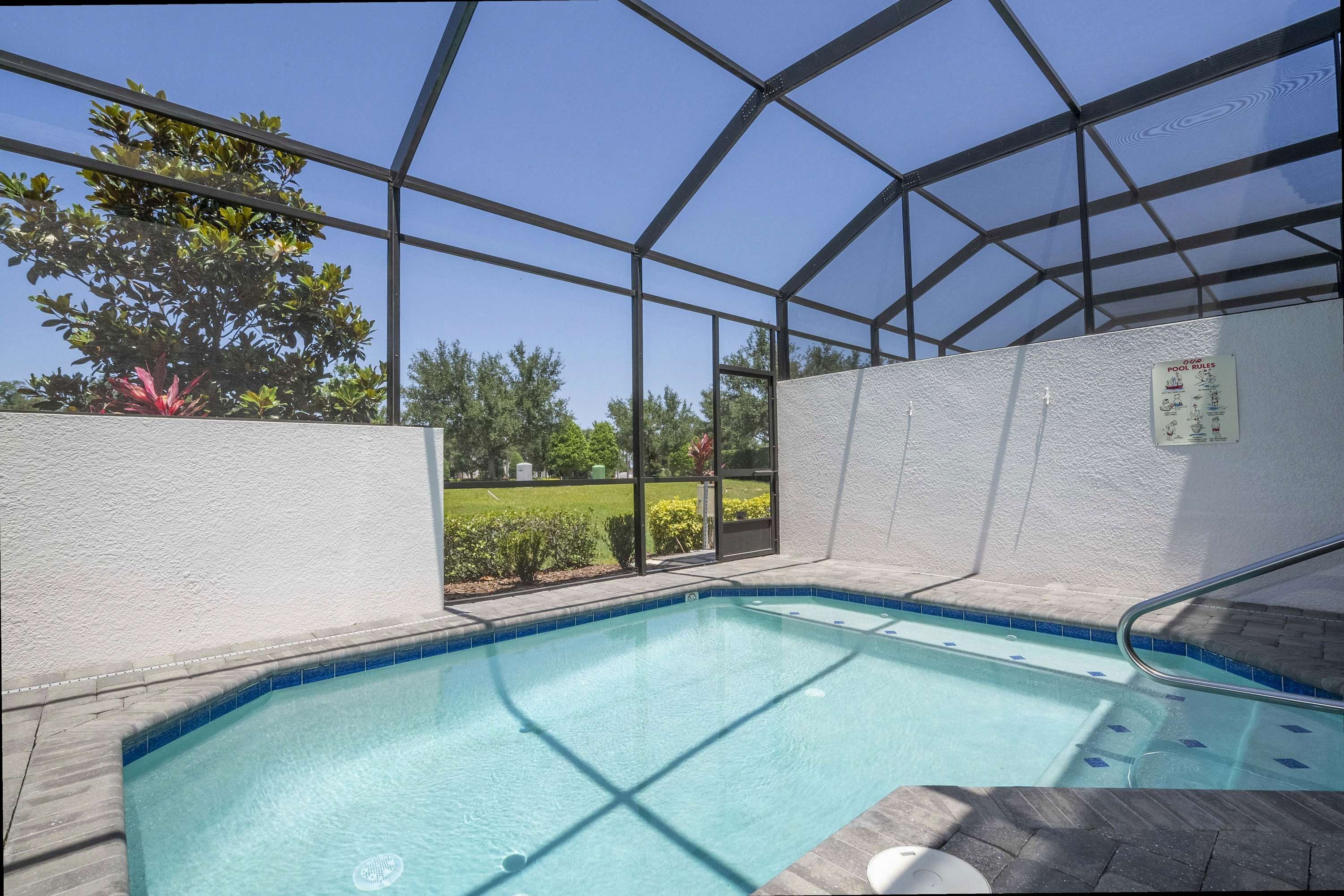 A covered swimming pool with clear blue water, surrounded by a white wall and a glass enclosure.