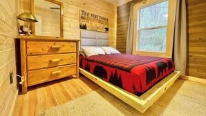 A wooden cabin bedroom with a bed, dresser, and a window. - Cozy cabin! Great Location! (Sevierville)