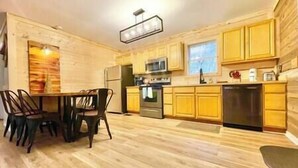 A modern kitchen with wooden cabinets, a dining table with chairs, and a built-in oven. - Cozy cabin! Great Location! (Sevierville)