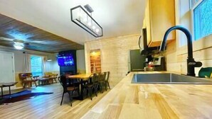 A modern kitchen with a wooden floor, a built-in sink, and a dining area with chairs and a table. - Cozy cabin! Great Location! (Sevierville)