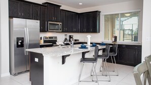 A modern kitchen with dark cabinets, stainless steel appliances, a granite countertop, and a bar area with stools.