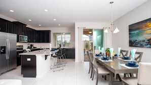 A modern kitchen with dark cabinets, a stainless steel refrigerator, and a dining area with a long table set for six.