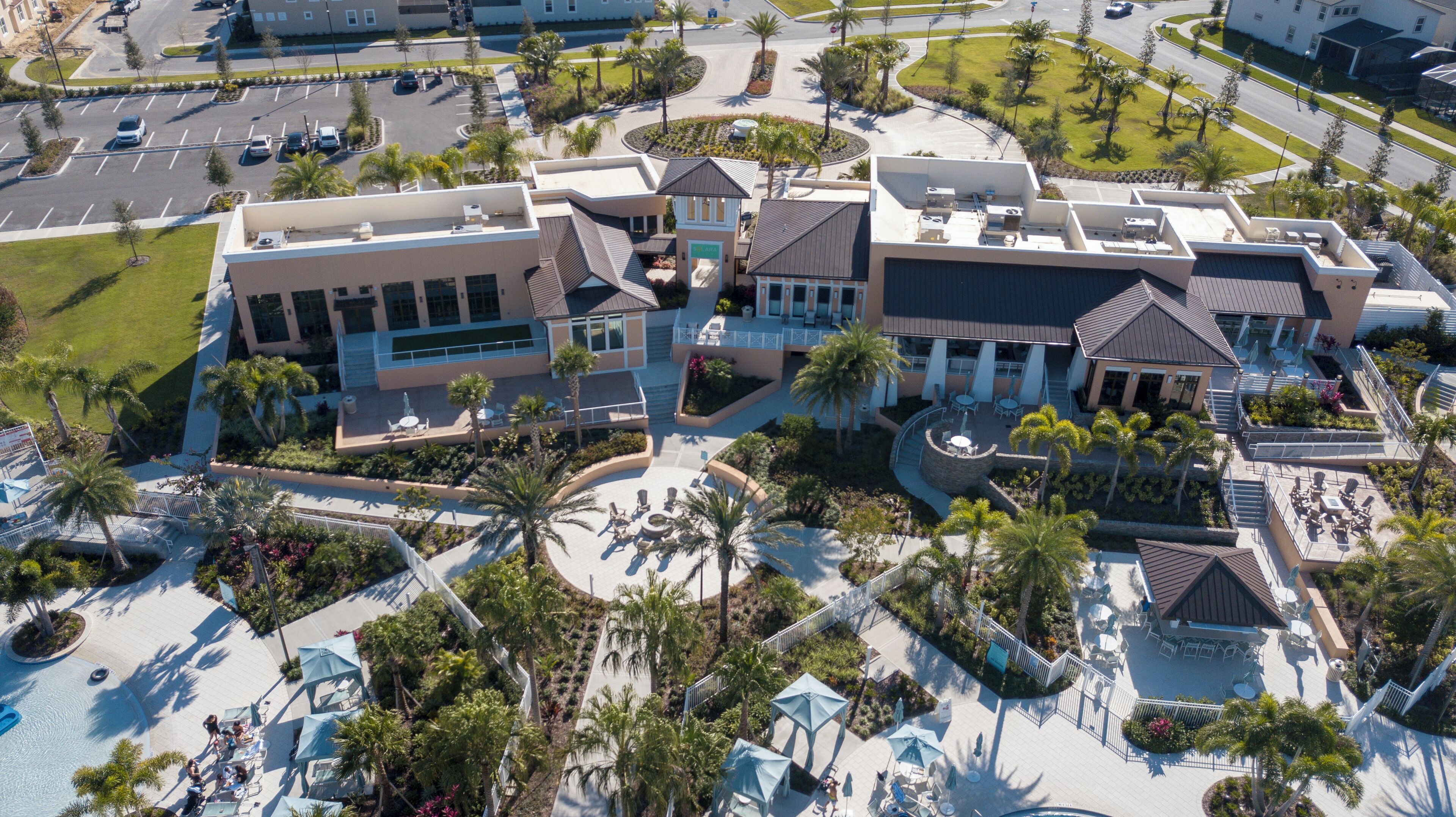 An aerial view of a hotel with multiple buildings, a central courtyard with palm trees, and a swimming pool area.