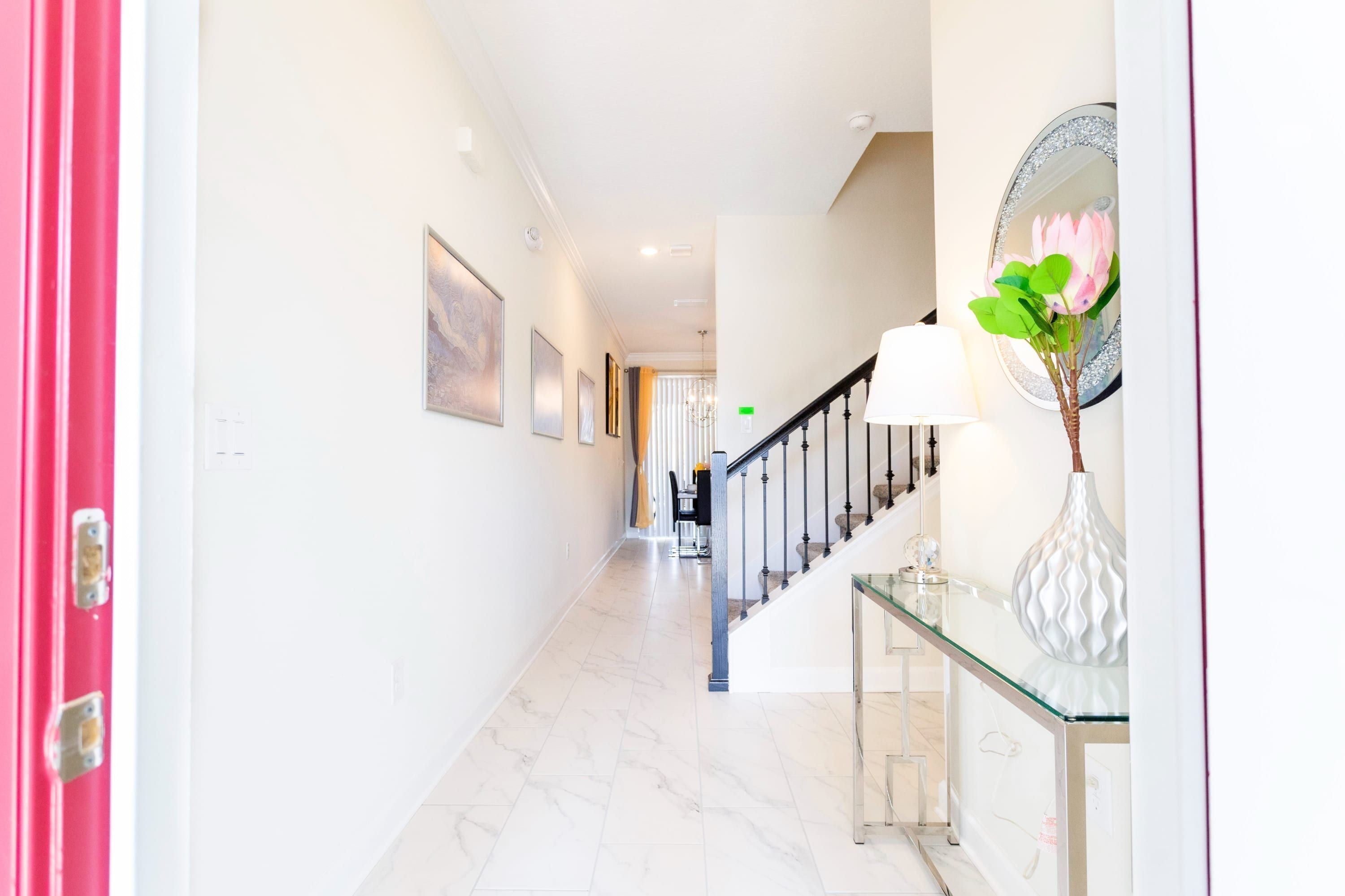 A hallway with a marble floor, a staircase with a glass railing, and a vase with flowers on a console table.