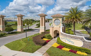 A gated entrance with a sign reading 'ChampionsGate,' a road leading through, and well-maintained landscaping.