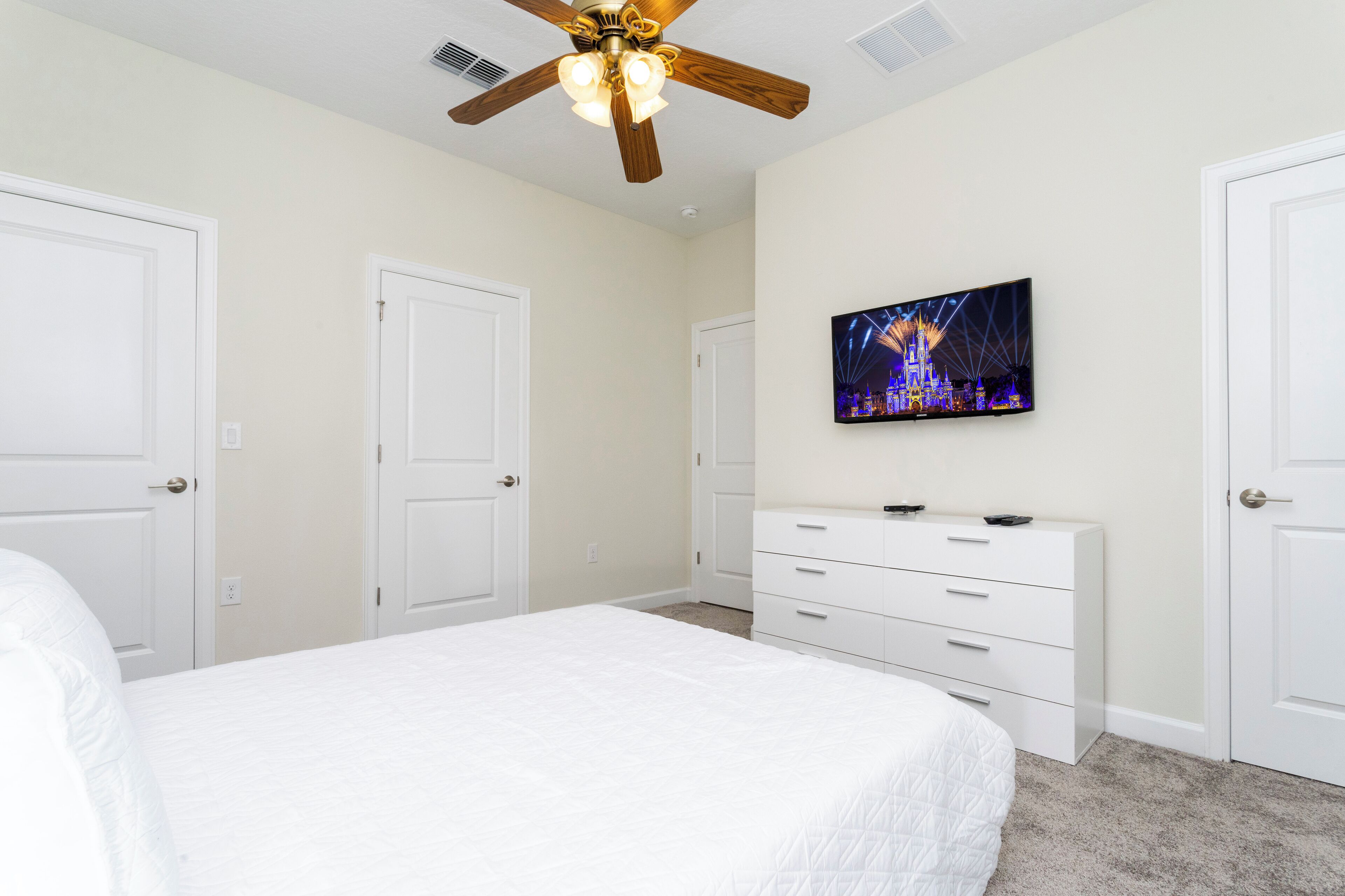 A bedroom with a bed, a ceiling fan, a dresser, and a TV on the wall.