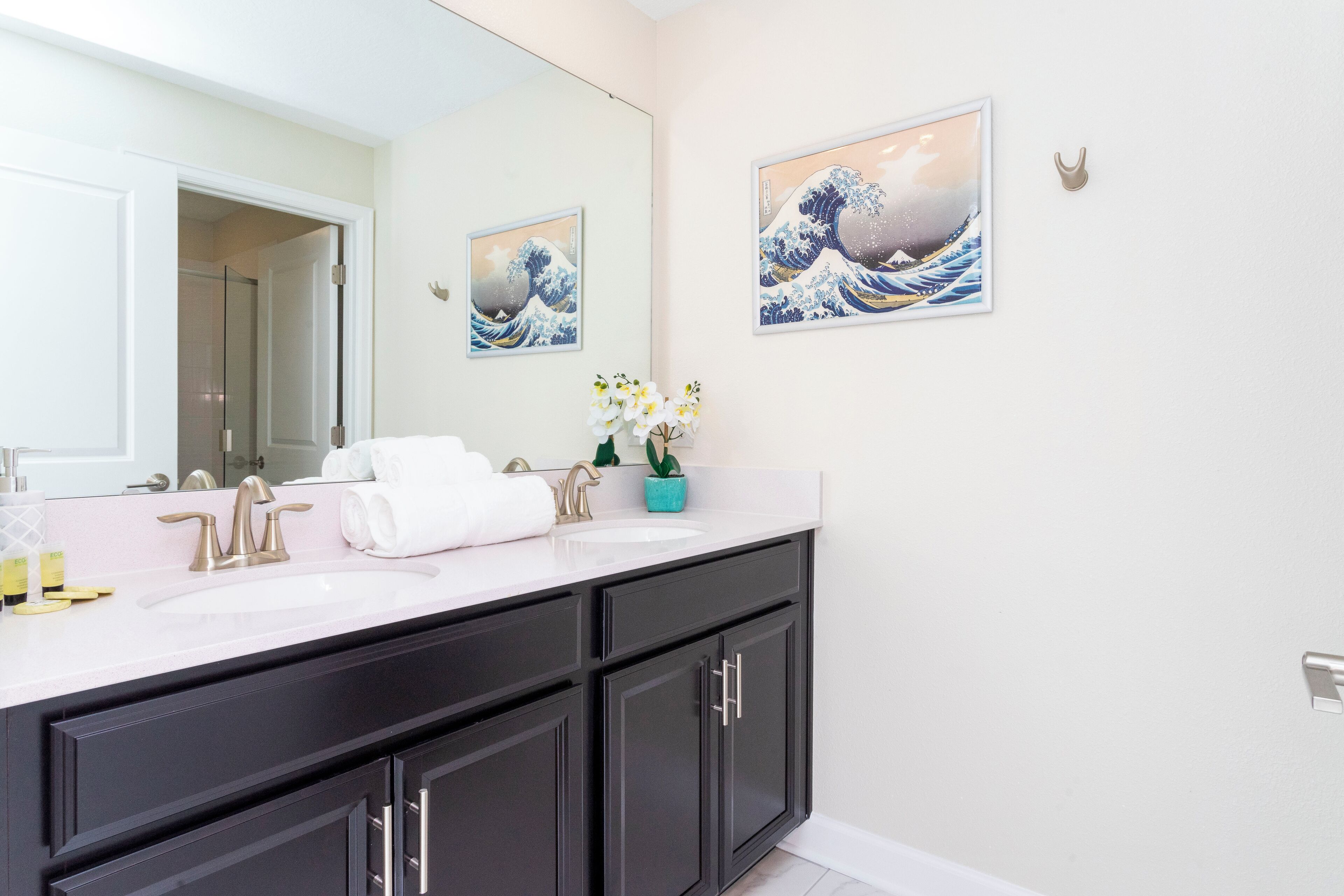 A modern bathroom with a large mirror, two sinks, dark cabinets, and artwork on the walls.