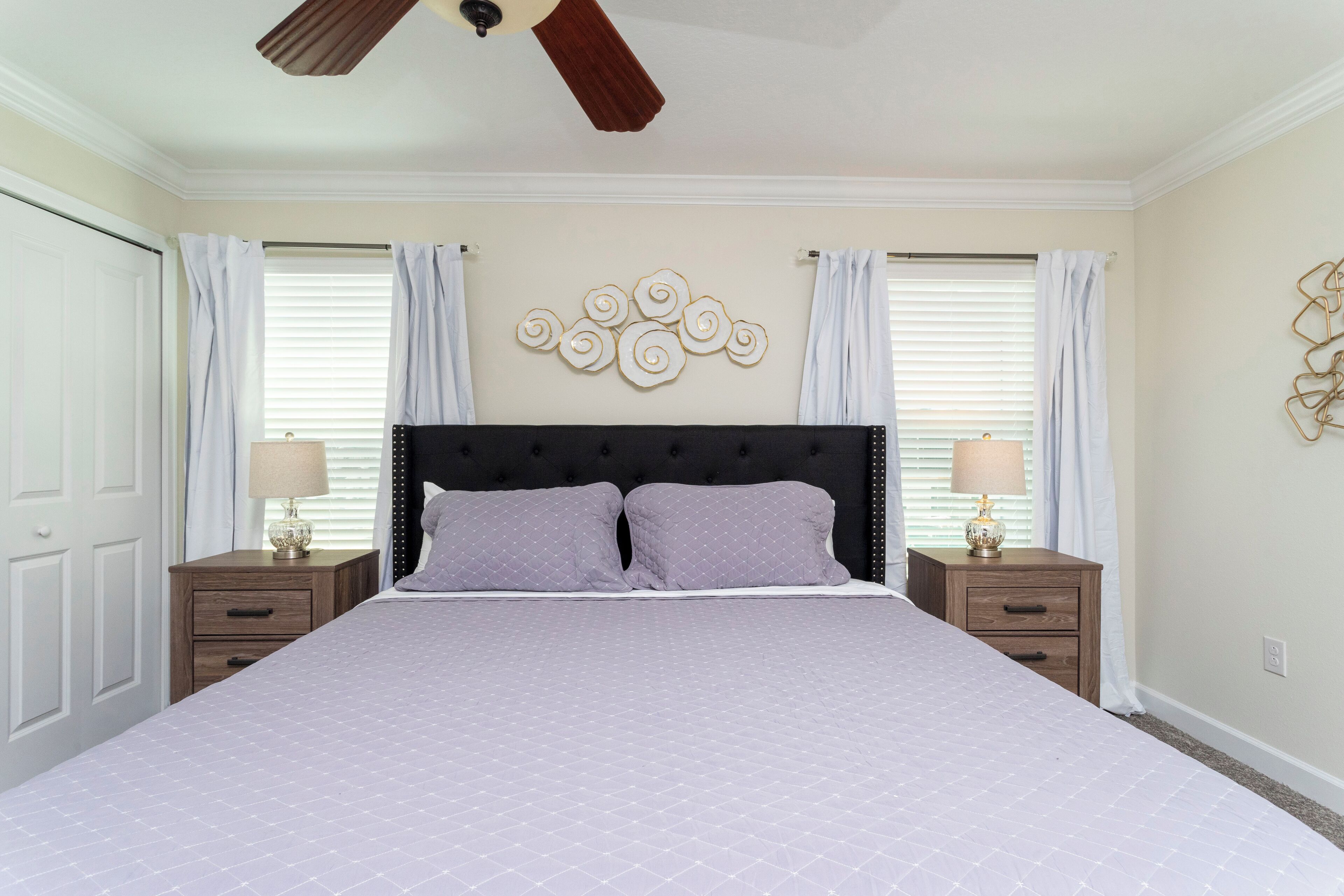 A bedroom with a large bed, two bedside tables, a ceiling fan, and a decorative wall piece.