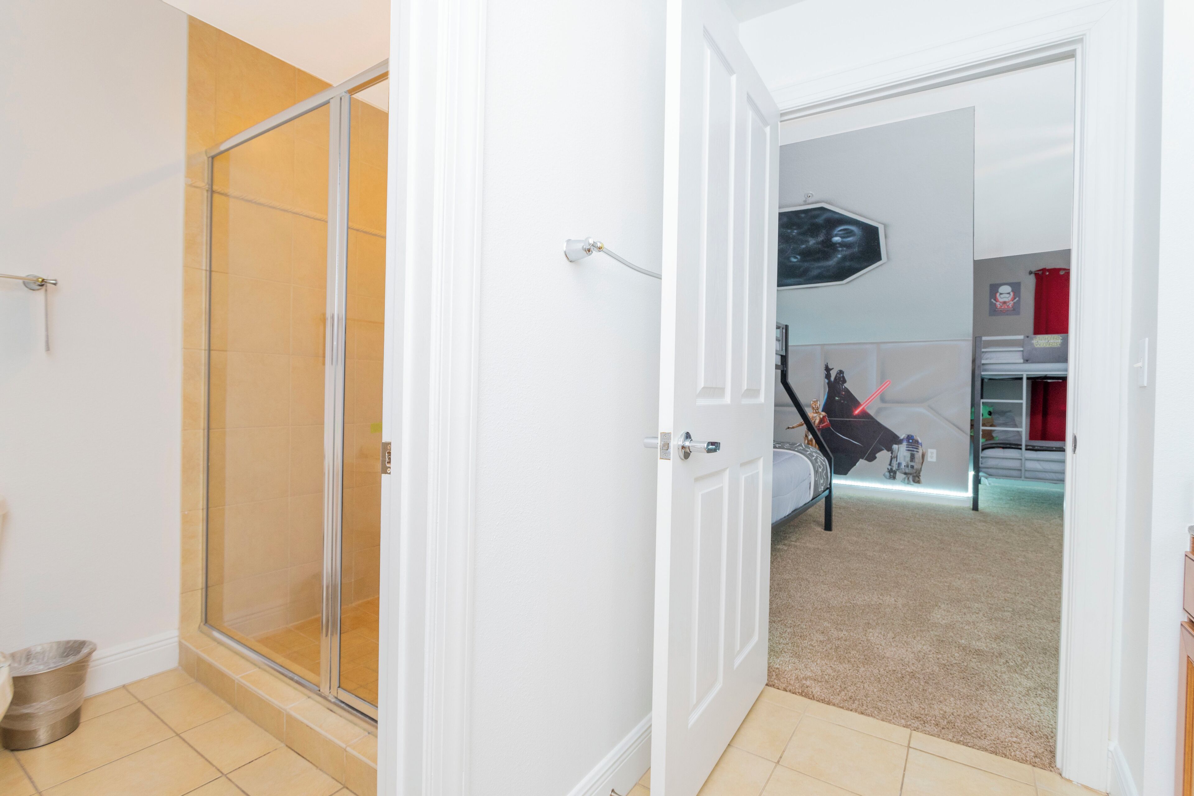 A room with a glass shower door, a bed with a Star Wars-themed wall art, and a red curtain.