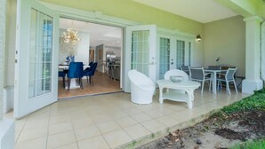 Un patio couvert avec une table et des chaises, une baignoire blanche et une vue sur l’intérieur de la maison.