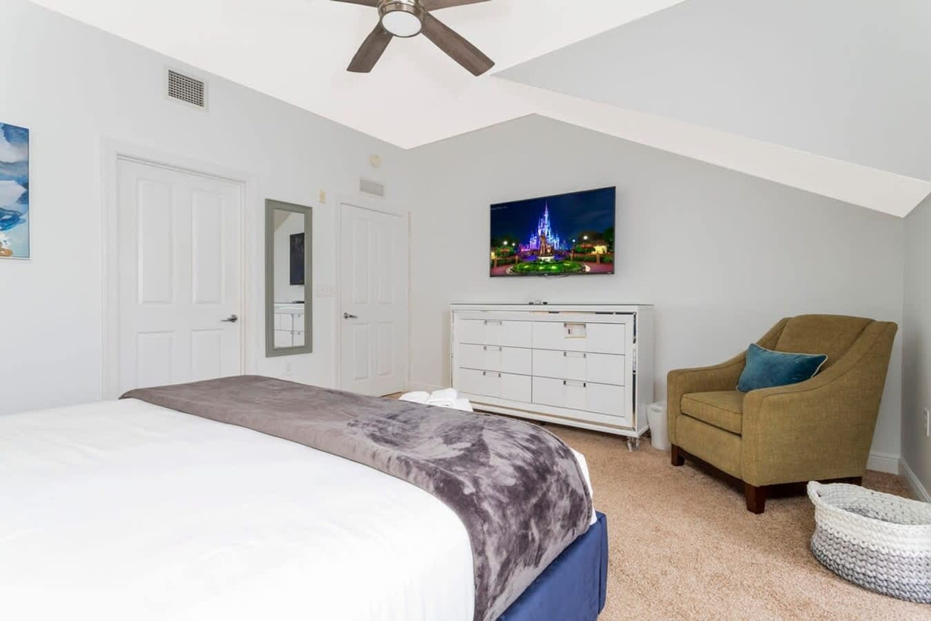 Ein Schlafzimmer mit einem Bett, einem Schminktisch, einem Sessel und einem Fernseher an der Wand.