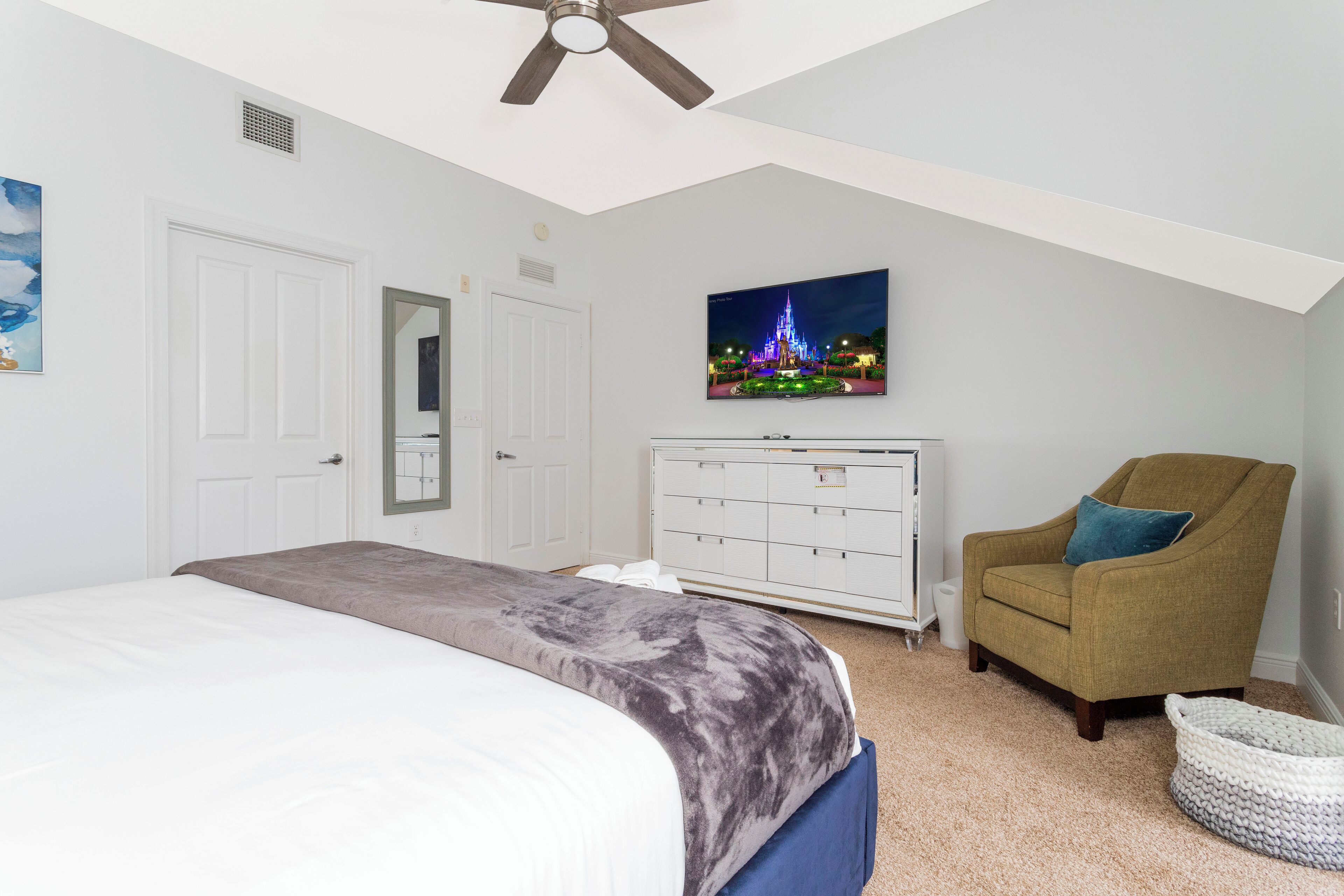 A bedroom with a bed, a dresser, a chair, a TV, and a ceiling fan.