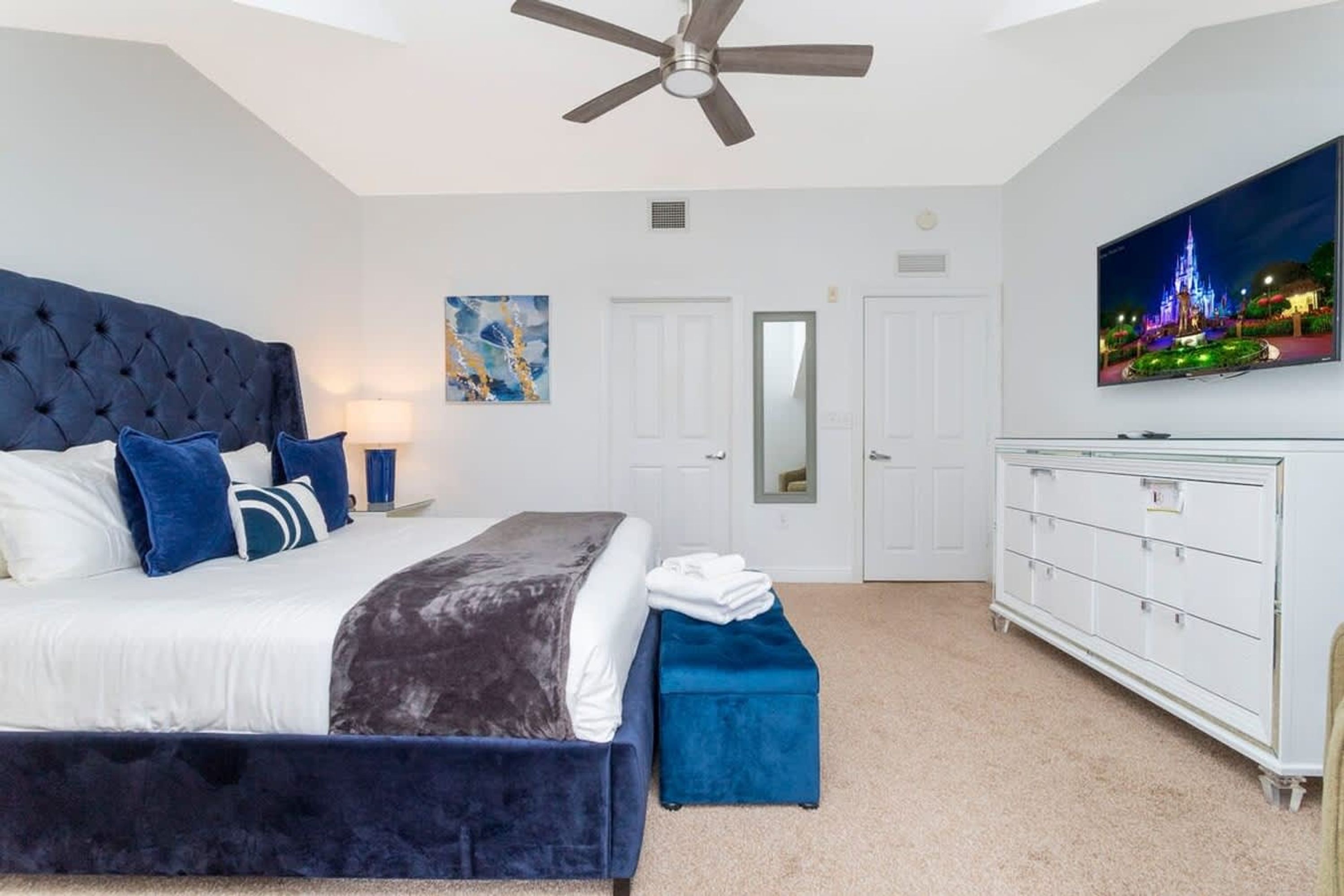 A bedroom with a bed, a ceiling fan, a TV, a dresser, and a door.