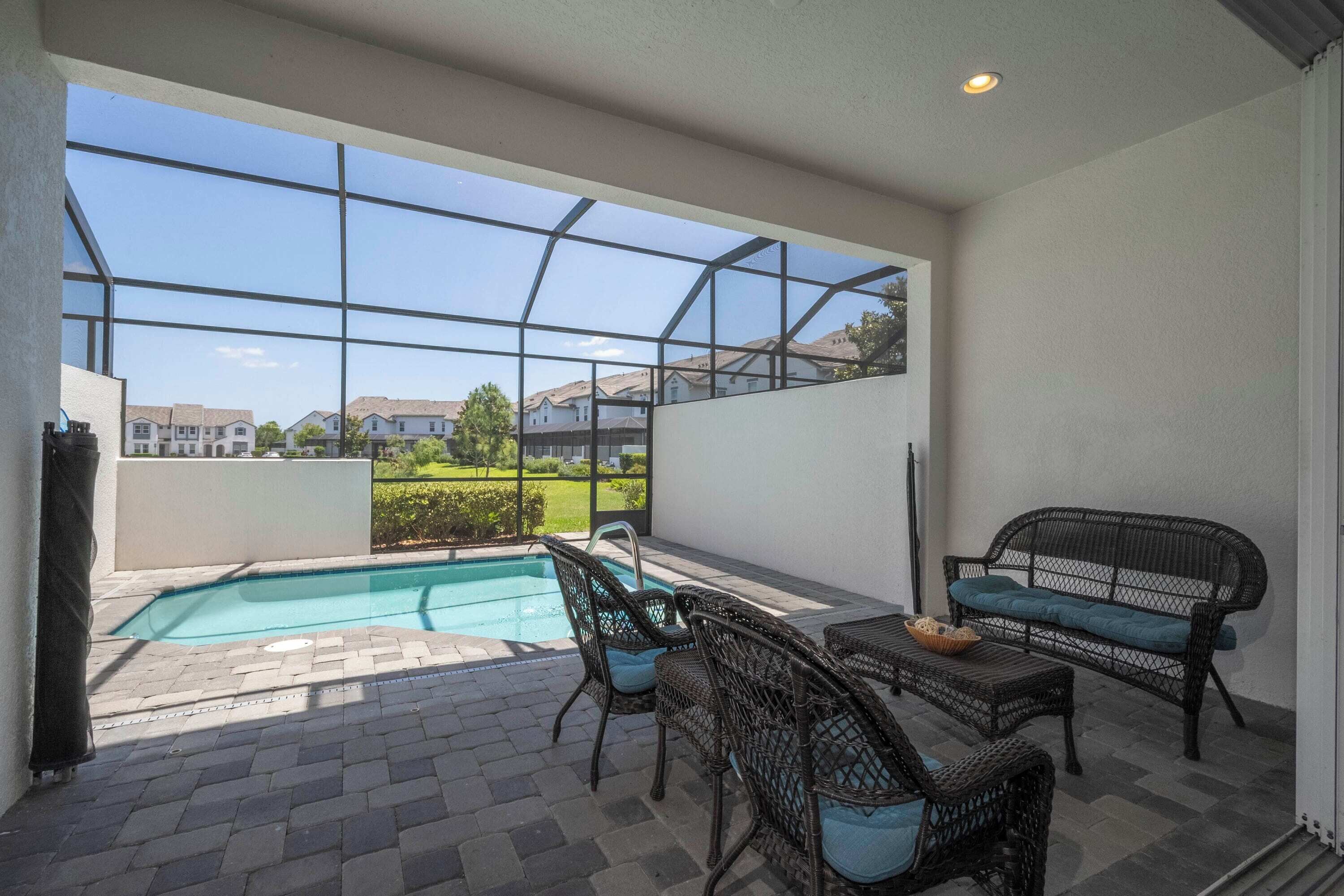 A spacious patio with a swimming pool, wicker furniture, and a glass enclosure offering a view of the neighborhood.