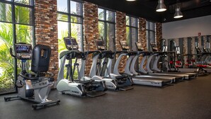 Ein Fitnessstudio mit Laufbändern, Crosstrainern und einer Ziegelwand mit großen Fenstern.