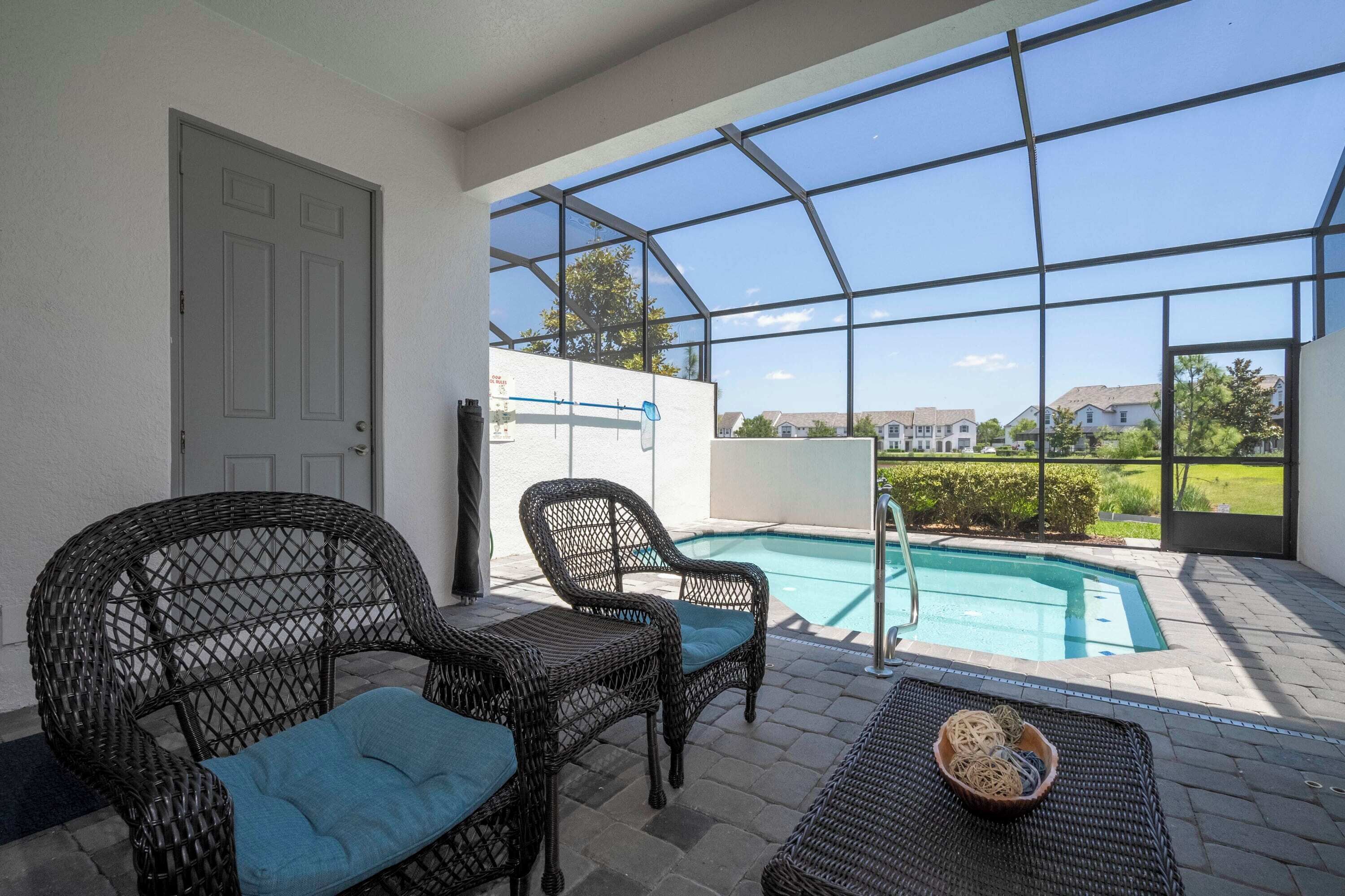 A covered patio with wicker furniture, a pool, and a view of houses in the background.