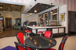 Interior de restaurante com área de bar, cadeiras vermelhas e mesa preta.