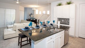 A modern kitchen with a central island, white cabinetry, and a dining area with a white sofa and coffee table. - Festival Resort 5 Bd Home w Screened Pool Close to Disney 174 (Davenport)